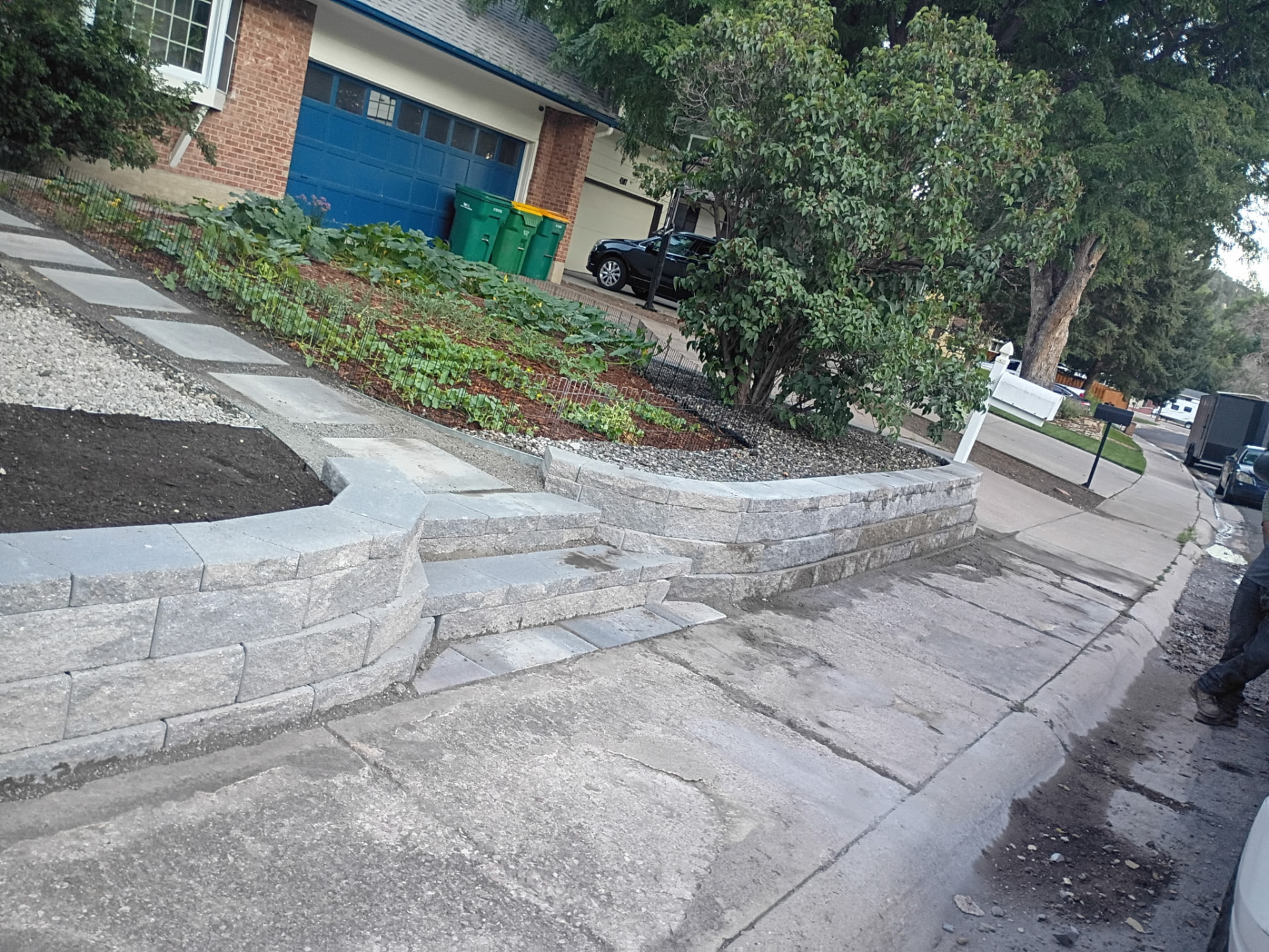 Block retaining wall with integrated steps along a residential driveway.